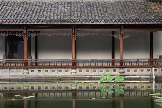 Traditional Chinese garden corridor with tiled roof and wooden pillars reflected in a quiet pond with green lotus leaves