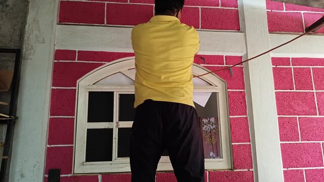 Young man wiping wall column with damp cloth indoors