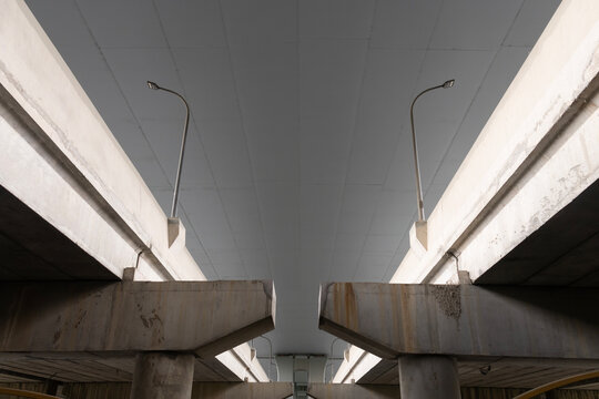 Symmetrical low angle view under a concrete highway overpass bridge with street lights