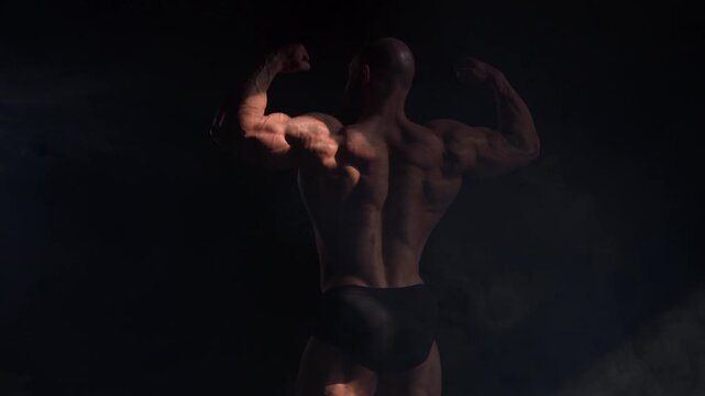 A male bodybuilder poses in shorts, showing off his back muscles.