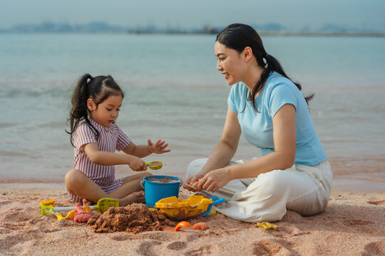 happy preschool child girl playing sand toy with mother on sea beach in Pattaya, Thailand