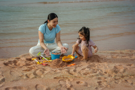 happy preschool child girl playing sand toy with mother on sea beach in Pattaya, Thailand