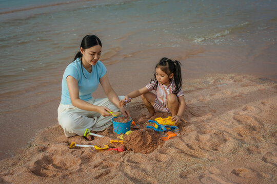 happy preschool child girl playing sand toy with mother on sea beach in Pattaya, Thailand