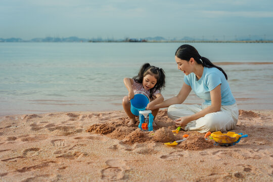 happy preschool child girl playing sand toy with mother on sea beach in Pattaya, Thailand