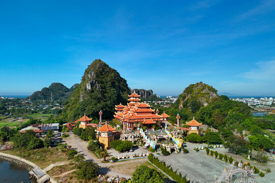 Bright orange Buddhist pagoda architecture surrounded by lush green limestone mountains and rural landscape under a clear sunny sky in Da Nang Vietnam