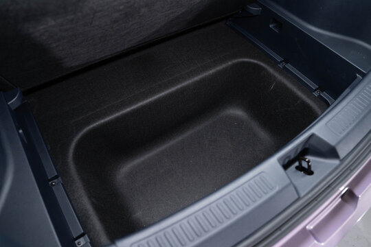 Rear storage compartment beneath trunk floor lined with dark material and molded panels. Recessed design with latch mechanism highlights utility and organization. 