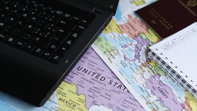 Detailed view of black laptop with a politic world maps and a passport at background in a planning vacations concept