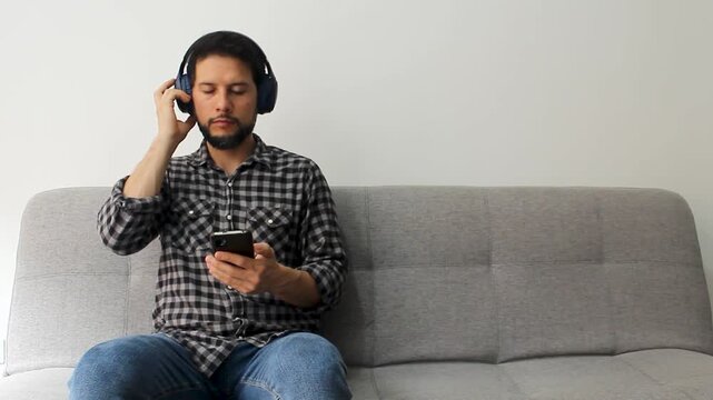 A hispanic man with bear and the eyes closed at the left side of the screen enjoying deeply listen music with a smartphone and a headset