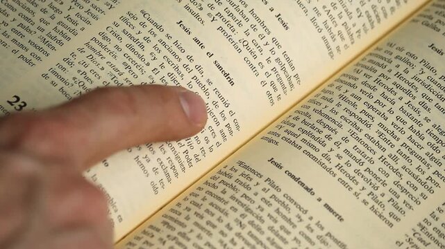 Detail view with selective focus of a male hand pointing with his index finger to a text passage of the holy bible in spanish