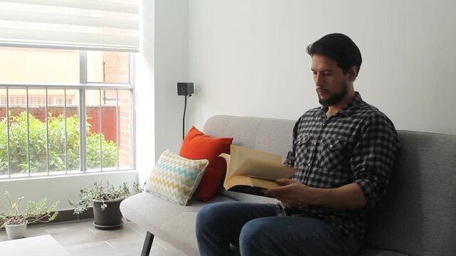 Detailed view of a latin man sitting on a couch leafing a text book in a concentrated attitude