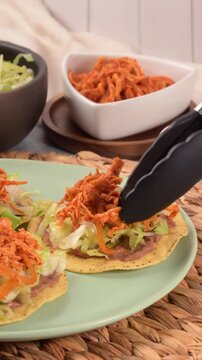 Hand prepares a Mexican tostada with chicken tinga