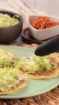 Hand prepares a Mexican tostada with fresh lettuce