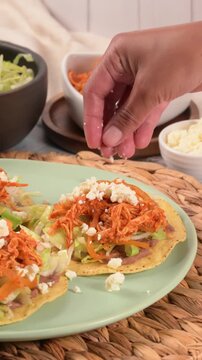 Mexican Chicken Tostadas Preparation. Hand prepares a Mexican tostada with crumbled cheese
