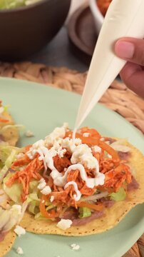 Preparing Mexican food. Woman&acute;s hand putting sour cream on top of a crispy chicken tostada