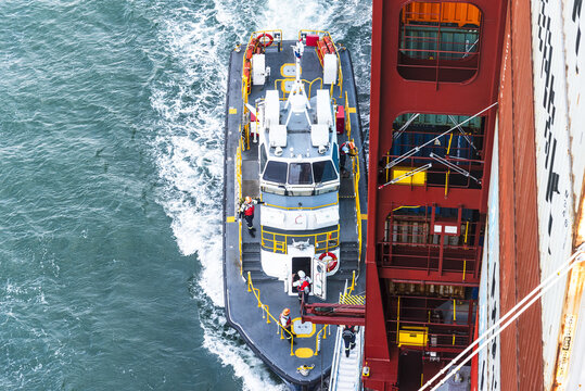 Pilot boat navigating alongside a large container ship during a crew transfer operation. Safe personnel transfer between vessels in commercial shipping.