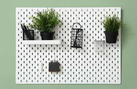 White pegboard with stationery, eyeglasses and plants hanging on color wall