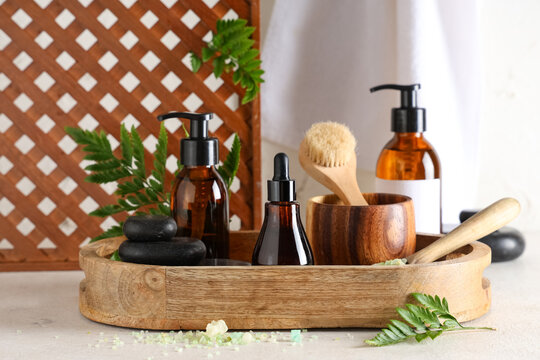 Wooden board with cosmetic products, spa accessories and fern leaves on light table