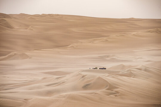 Panoramic desert dunes with distant vehicles and people, travel in Peru