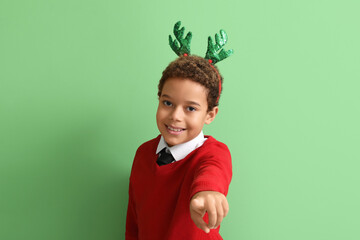Little African-American boy in reindeer horns pointing at viewer on green background © Pixel-Shot