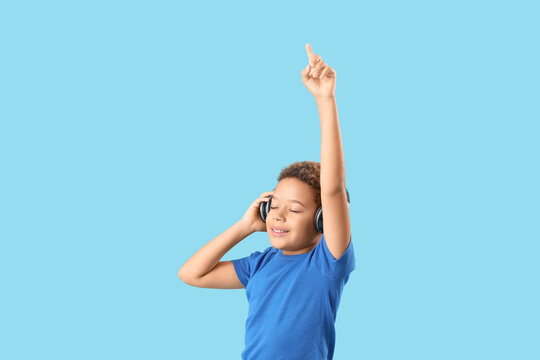 Little African-American boy with headphones listening to music on blue background