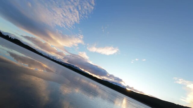 A tranquil view of Laguna La Zeta with smooth water reflecting clouds and distant snow-capped mountains near Esquel, Argentina at golden hour.