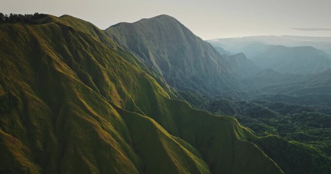 Sembalun vast green mountains, ridges, rolling hills with dense forest in highland valley under a serene sky. Beautiful natural landscape of Lombok island, Indonesia. Aerial view drone flight panorama