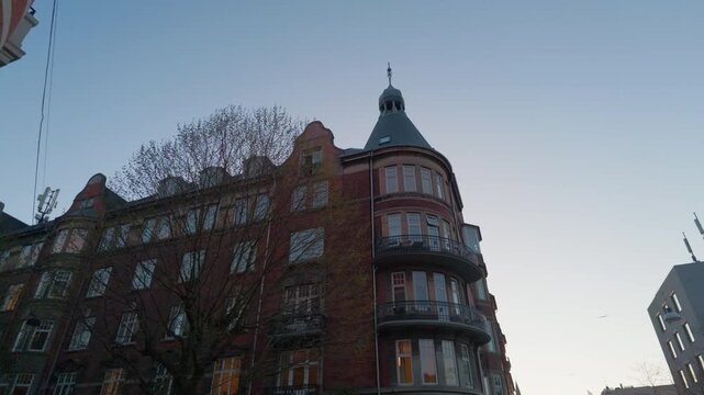 Red brick building sunset street, gimbal stabilizer shot. 60fps tilt up reveal walking on sidewalk looking at circular corner architecture in Copenhagen Denmark.
