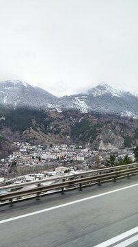 Passing view from bus of Modane town, snowy mountains, and highway in winter