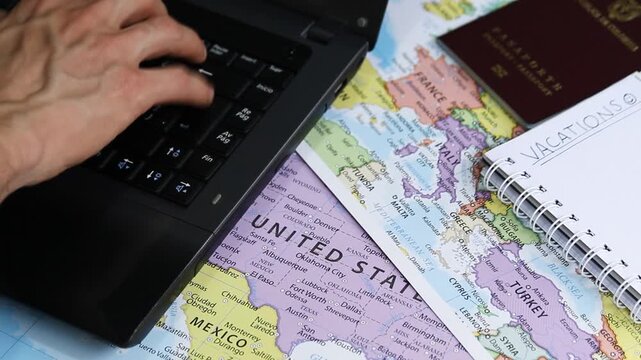 Detailed view of a male hand planning and searching on a laptop with a passport and a notebook near