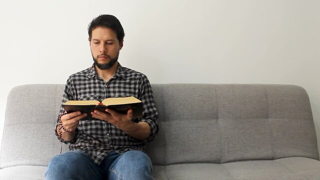 Detailed view of a latin believer man reading the holy bible with a rosary in his hand in a concentrating attitude