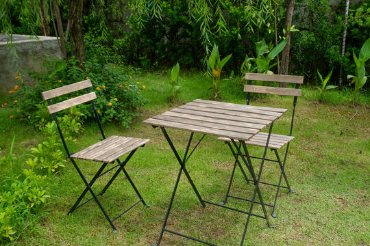 Wooden table and chair set in garden on a sunny day,outdoor seating for restaurant or cafe,Neat paved patio with sitting area and small garden in forest.