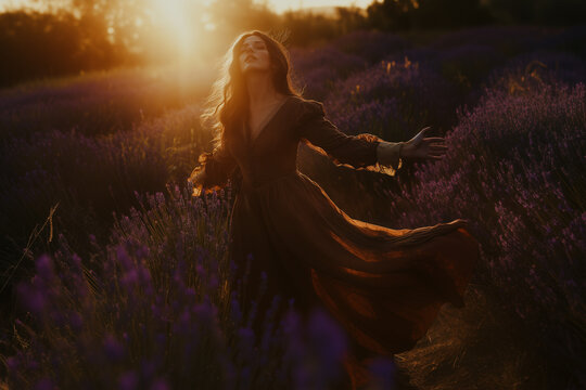 Young woman in a medieval brown dress dances in the light of the setting sun in a lavender field background.