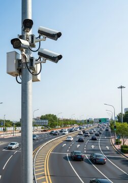 Multiple modern security cameras mounted on a tall metal pole overlooking a busy asphalt road to monitor traffic flow and urban safety, intersection, recording, outdoor