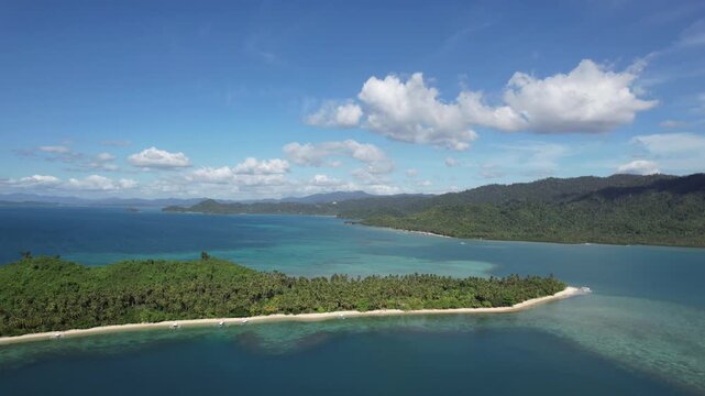 An isolated, uninhabited tropical island with a beach of crystal clear waters and white sand seen from afar. Palm trees and untouchable local flora. Filmed with a Drone in Palawan, Philippines, Asia.
