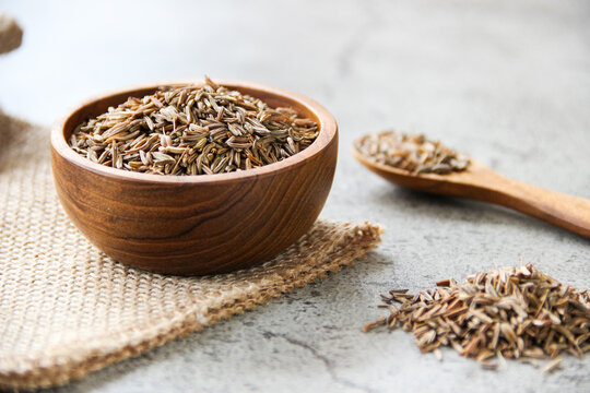 Caraway seeds in wooden bowl and spoon on gray concrete background