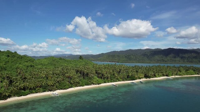 An isolated, uninhabited tropical island with a beach of crystal clear waters and white sand seen from afar. Palm trees and untouchable local flora. Filmed with a Drone in Palawan, Philippines, Asia.