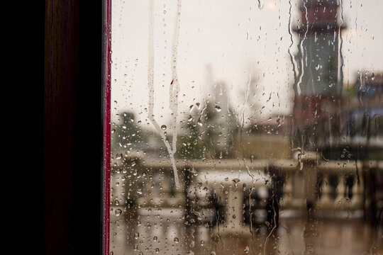 Raindrops trickle down the glass,Water Droplets on a pane of glass with blurred city background,View from a window showing rain falling rainy day,Copy space.