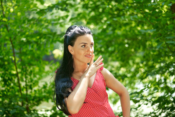 Fototapeta premium A young woman in a red polka-dot dress stands in a sunlit forest.