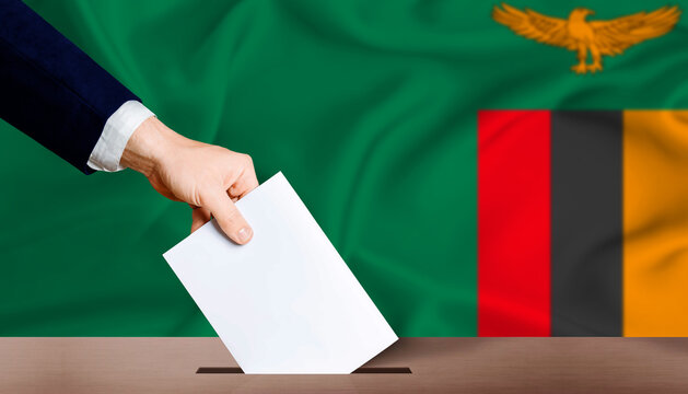 Hand placing a ballot in ballot box with the Zambian flag in the background. Zambia Presidential vote