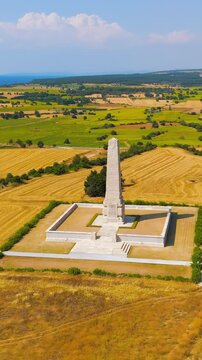 Vertical video. Seddulbahir, Eceabat, Turkey. Helles Memorial obelisk rising from a broad limestone base amid golden fields, aerial view over the Dardanelles under clear summer sky. Aerial View, Depa