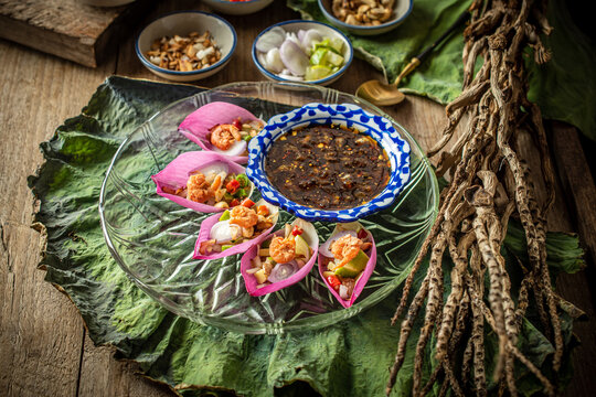 Delicious Miang Kham Bua Luan, a traditional Royal Thai appetizer featuring vibrant pink lotus petals, toasted coconut, fresh herbs, and sweet savory dipping sauce served on a wooden table.