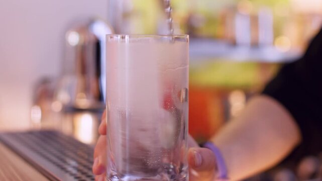 Refreshing cocktail making. Stirring ice. Bartender hand rotating frozen cube in tall glass with spoon on pub counter. Cooling for refreshing drink.