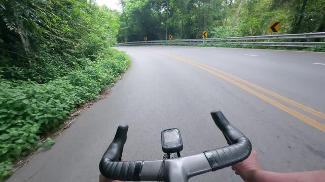 First-person POV footage of a road cyclist descending a winding mountain road surrounded by lush tropical forest. Passing vehicles on a scenic mountain curve create an authentic transportation atmosph