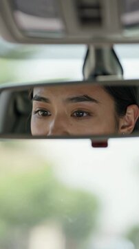 Close-up of a woman&rsquo;s eyes visible in the rearview mirror of a car, with her eyebrows raised and a focused expression, vertical shot