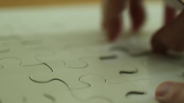 Horizontal 4K close up video of human fingers taking apart a blank white jigsaw puzzle removing pieces one by one on a table