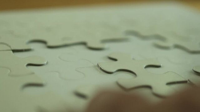Horizontal 4K close up video of hands trying to find the right spot and connect an unmatched blank white jigsaw puzzle piece