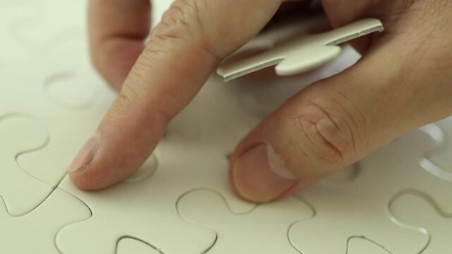 Horizontal 4K video of male hands placing remaining plain white jigsaw puzzle pieces filling every gap until complete
