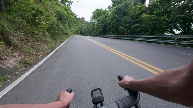 First-person POV footage of a cyclist descending a smooth winding mountain road through a lush tropical forest. The clean asphalt, sweeping left-hand curve, and immersive rider perspective create a ci
