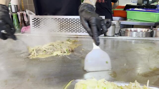 Chef Cooking Meat And Onions On Hot Teppanyaki Grill Close-up of a chef using metal spatulas to cook sliced meat and onions on a steaming hot teppanyaki griddle.