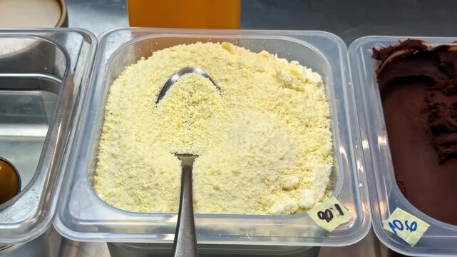 Ice cream toppings in plastic tubs with chocolate, cereal, and sweet sauces on display by scoop